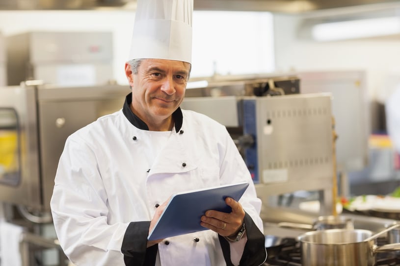 Chef using his digital tablet and looking at camera in the kitchen