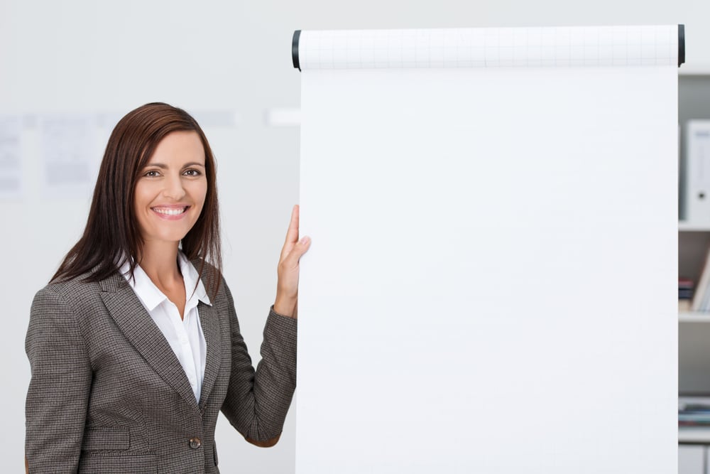 Confident happy businesswoman doing a presentation standing alongside a blank flipchart with white paper and copyspace for your text