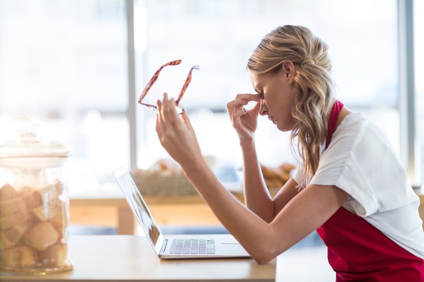 Tired waitress sitting at table and using laptop in cafx92xA9